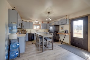 A kitchen with grey cabinets, a black refrigerator, a wooden dining table, and a water dispenser. - Cast, Catch & Relax: Craig Home, Step to River (Wolf Creek)