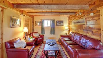 Interior acogedor de una cabaña con paredes de madera, un sofá de cuero rojo, un sillón a juego, una mesita de centro y una chimenea.