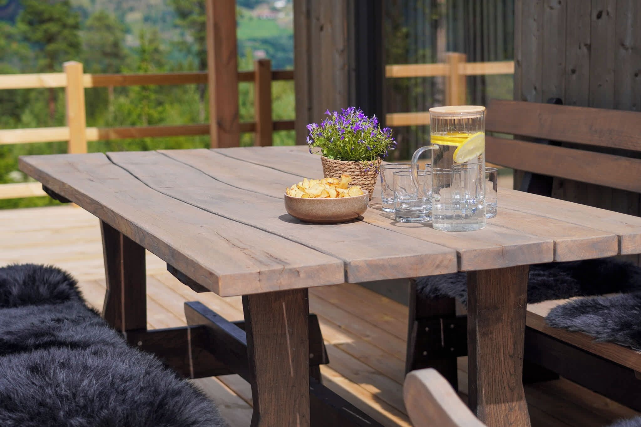 A wooden table with a bowl of chips, a glass of water with a lemon slice, and a potted plant with purple flowers.