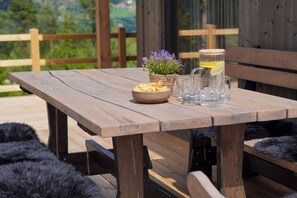 A wooden table with a bowl of chips, a glass of water with a lemon slice, and a potted plant with purple flowers.