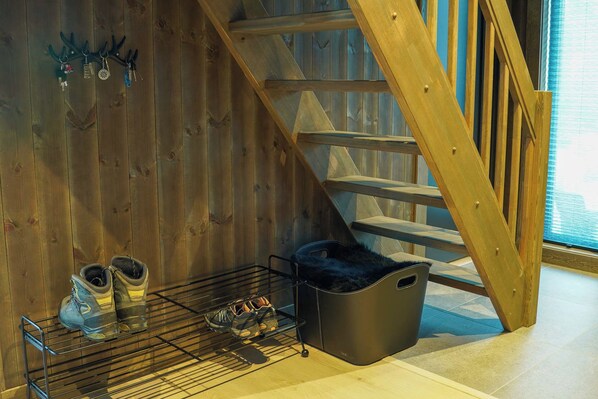 A wooden staircase, a shoe rack with boots, and a black storage bin.