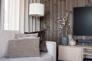 Un salon avec un canapé, des coussins, une lampe, un téléviseur et des vases décoratifs.