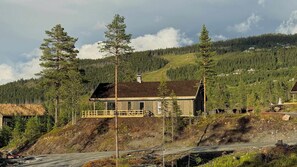 A wooden cabin with a balcony, surrounded by a forested hillside.