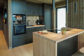 Une cuisine moderne avec des meubles de couleur sombre, un four encastré et un îlot central en bois doté d’un évier et d’une plante en pot.