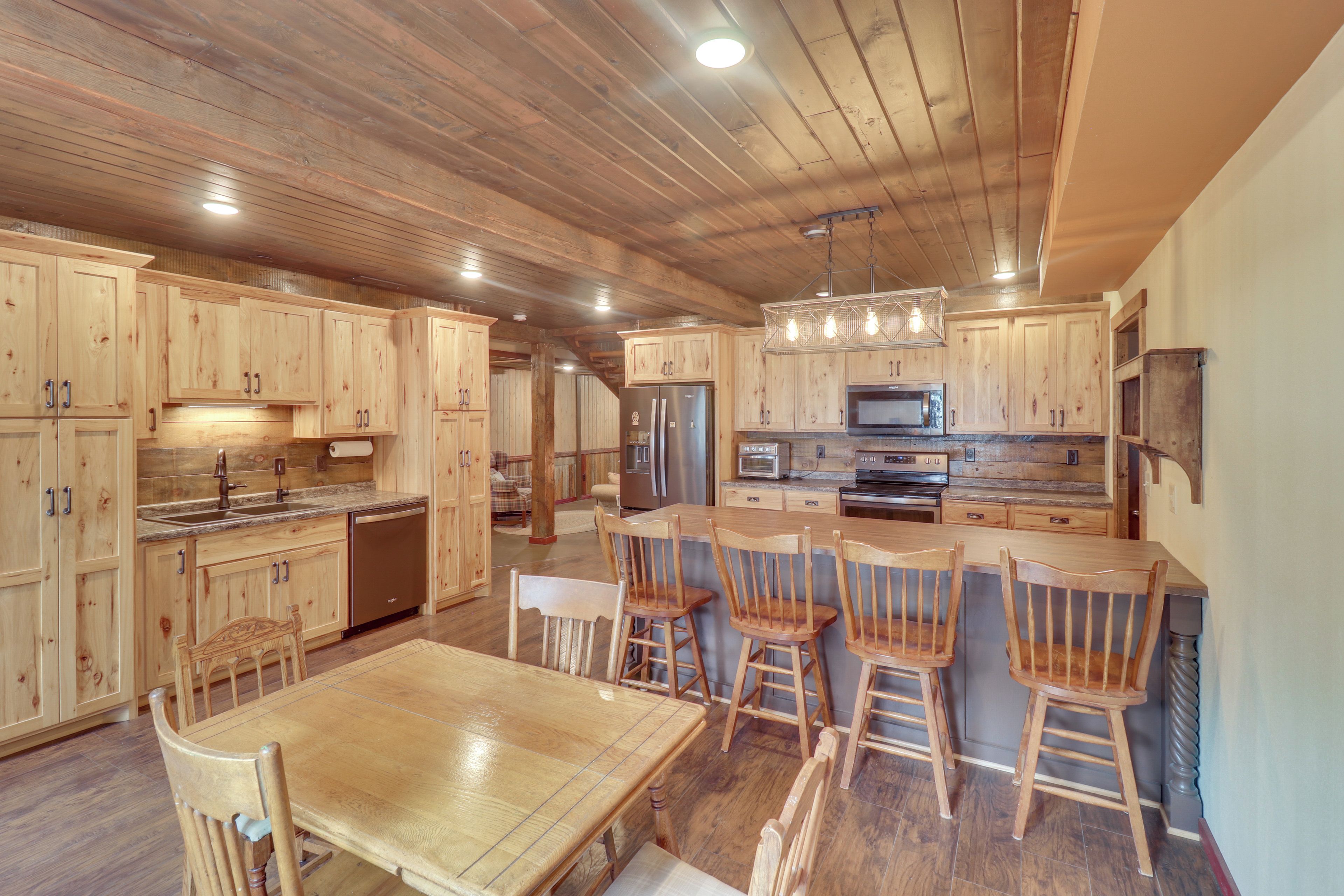 A spacious kitchen with wooden cabinets, a central island with bar stools, stainless steel appliances, and a hanging light fixture.