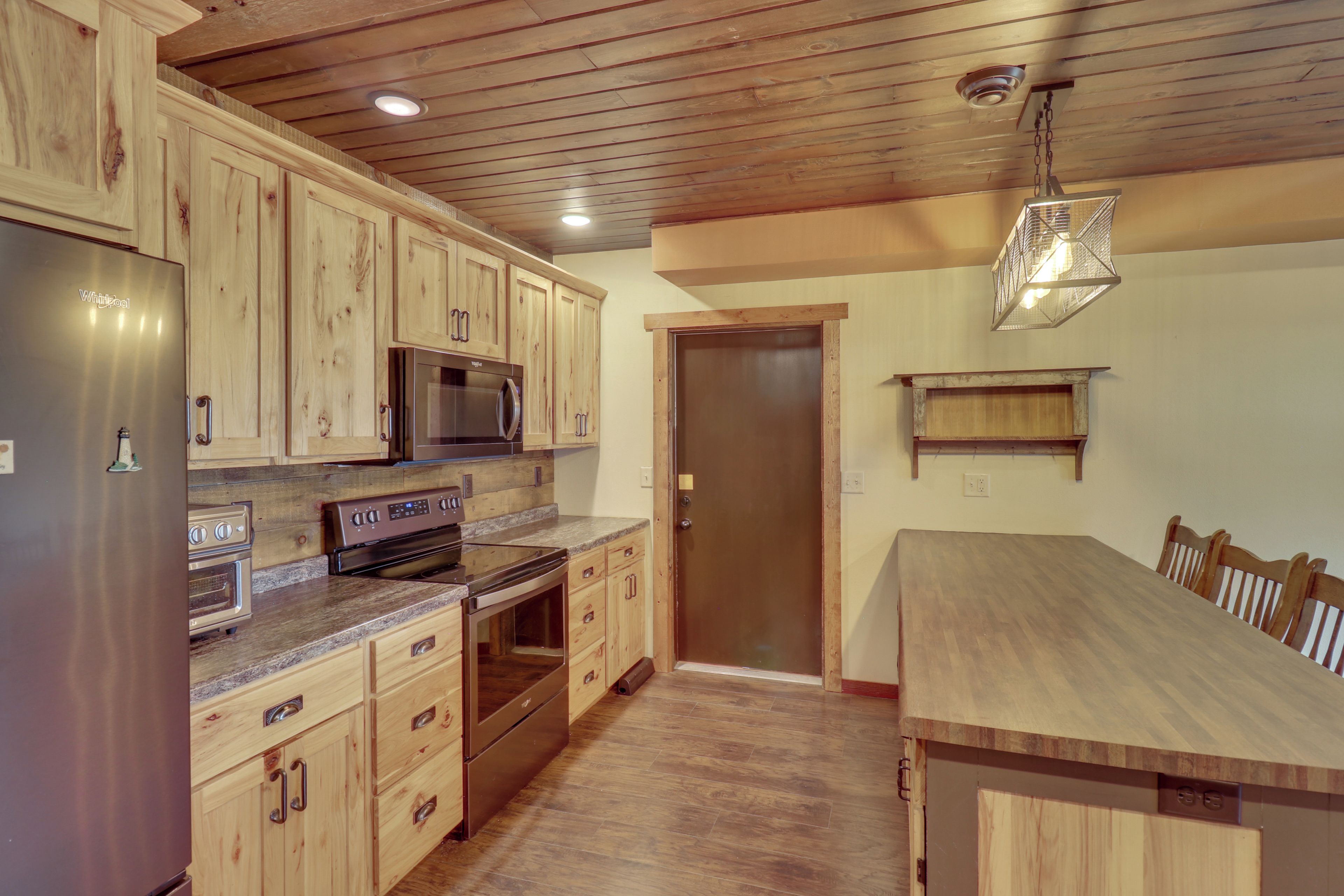 A kitchen with wooden cabinets, a stainless steel refrigerator, a microwave, an oven, and a dining table with chairs.