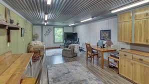 Un salón amplio con una gran televisión de pantalla plana, muebles de madera y vistas al exterior a través de una ventana.