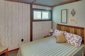 Un dormitorio con cabecera de madera, una ventana, una mesita de noche con lámpara y una pared decorada con marcos.