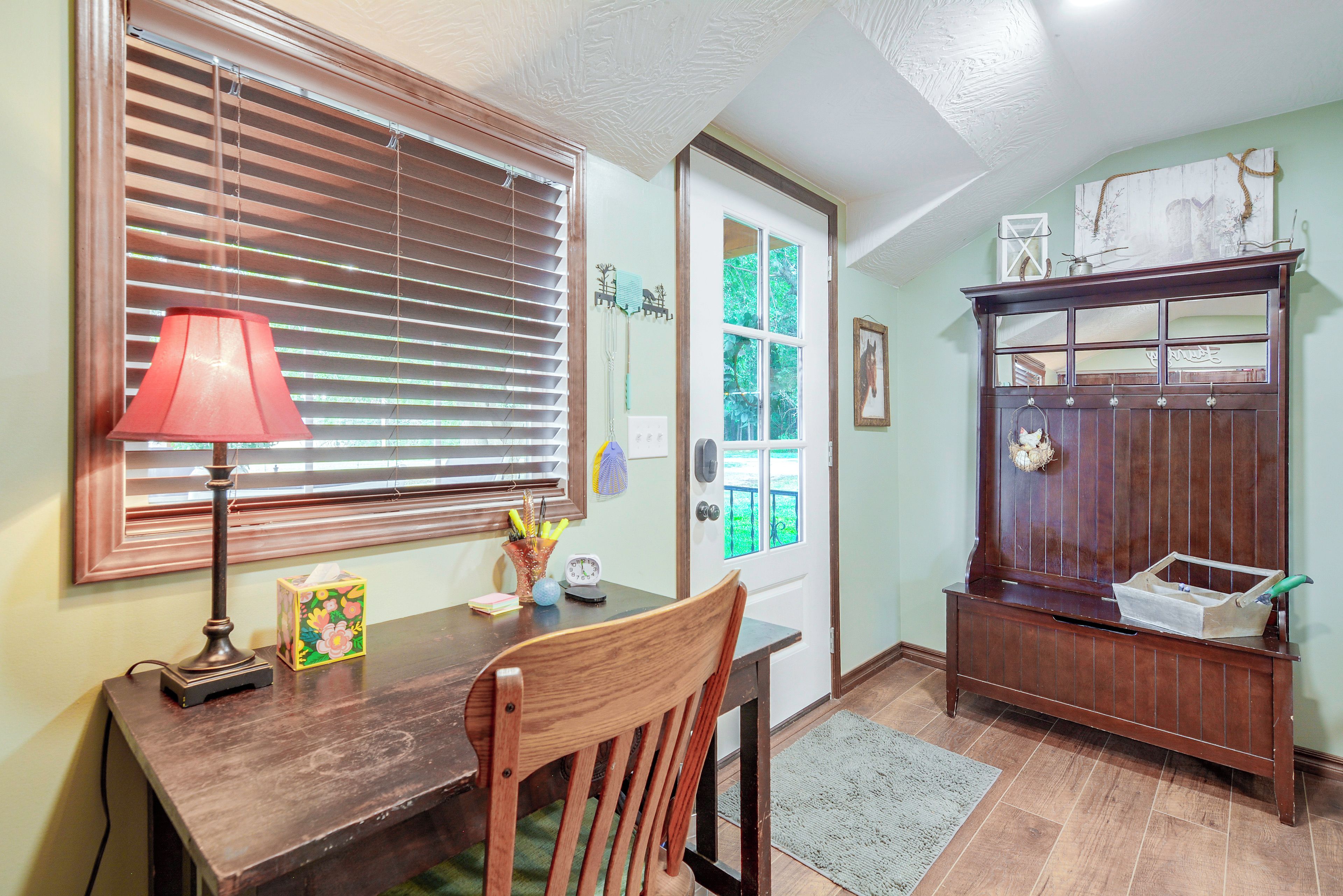 A room with a wooden desk, a chair, a lamp, a bookshelf, and a door leading outside.