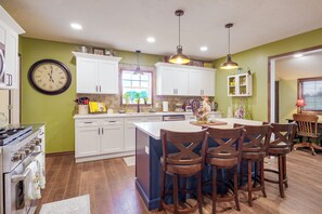 A kitchen with white cabinets, a large island with bar stools, a clock, and a window with a view. - Country Living! Fire Pit, Horse Stalls & Views (Verona)