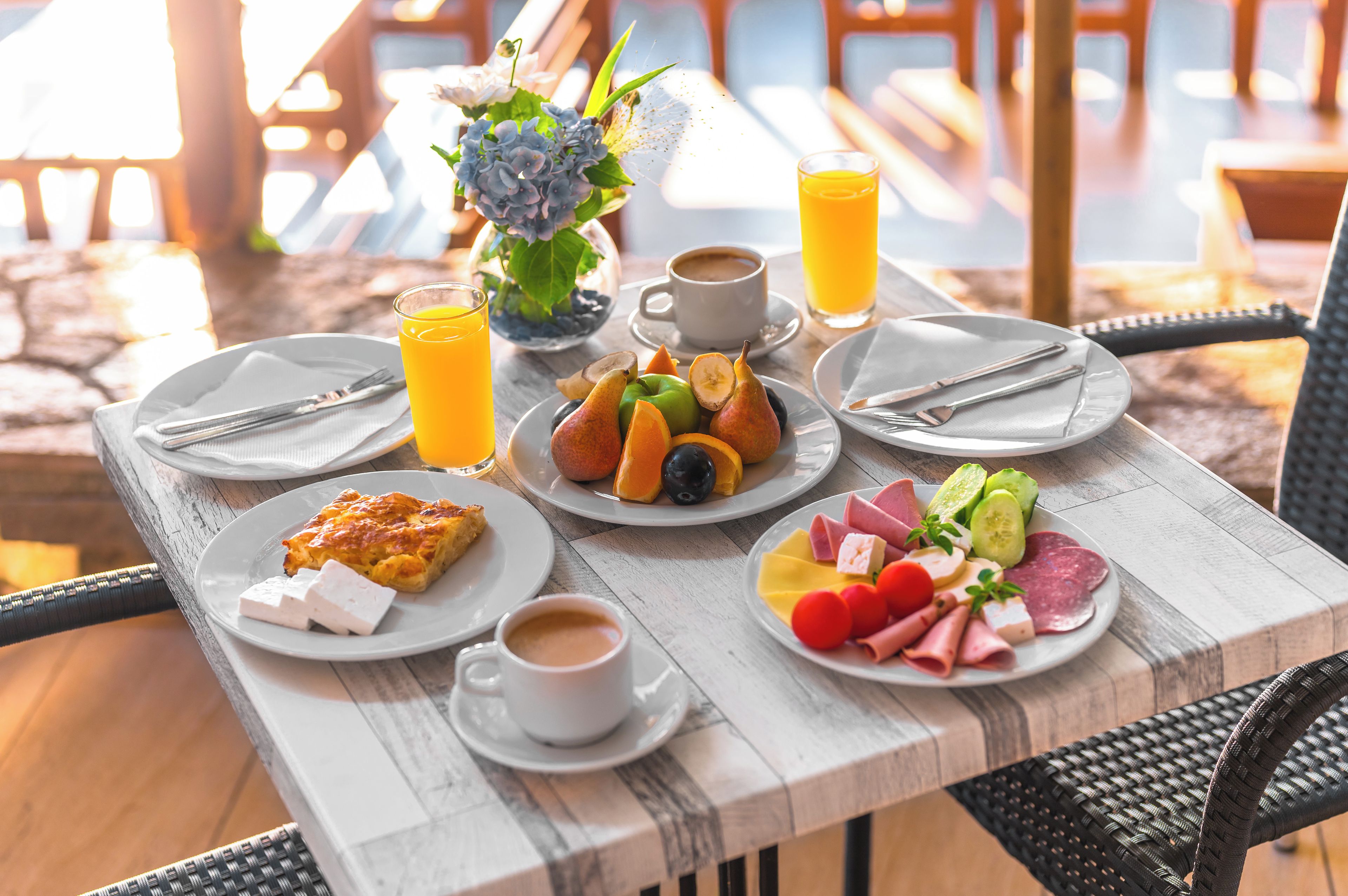 A table set with breakfast items including fruit, cheese, and ham, with a cup of coffee and a glass of orange juice.