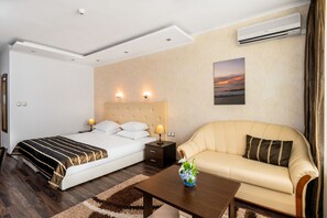 A hotel room with a bed, a sofa, a nightstand, an air conditioner, and a wall-mounted picture. - Kaliakra Palace (Varna)
