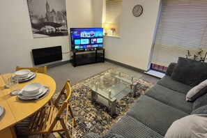 Ein Wohnzimmer mit einer Couch, einem Couchtisch, einem Fernseher und einem Essbereich mit Stühlen und Tellern.