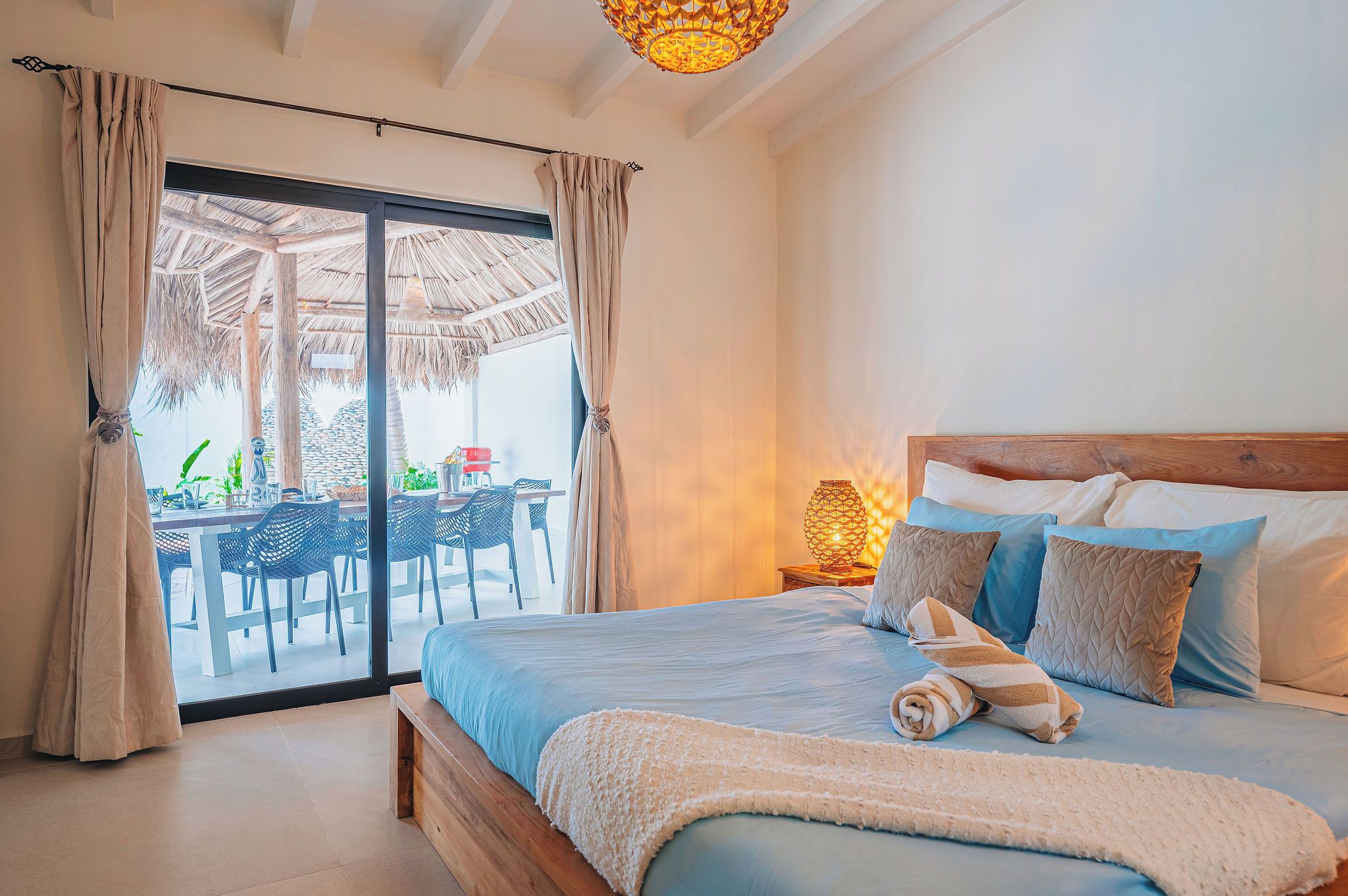 Un dormitorio con cama, almohadas, una mesita de noche y vistas a un área de comedor exterior.