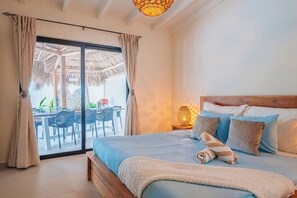 A bedroom with a bed, pillows, a nightstand, and a view of an outdoor dining area. - Your private Aruba escape with nearly everything brand new, 4 bedrooms, a tropical pool, waterfall wish spot, BBQ, and easy access to Palm Beach. (Noord)