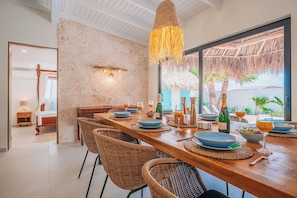 A dining area with a long wooden table set for six, surrounded by wicker chairs. - Your private Aruba escape with nearly everything brand new, 4 bedrooms, a tropical pool, waterfall wish spot, BBQ, and easy access to Palm Beach. (Noord)
