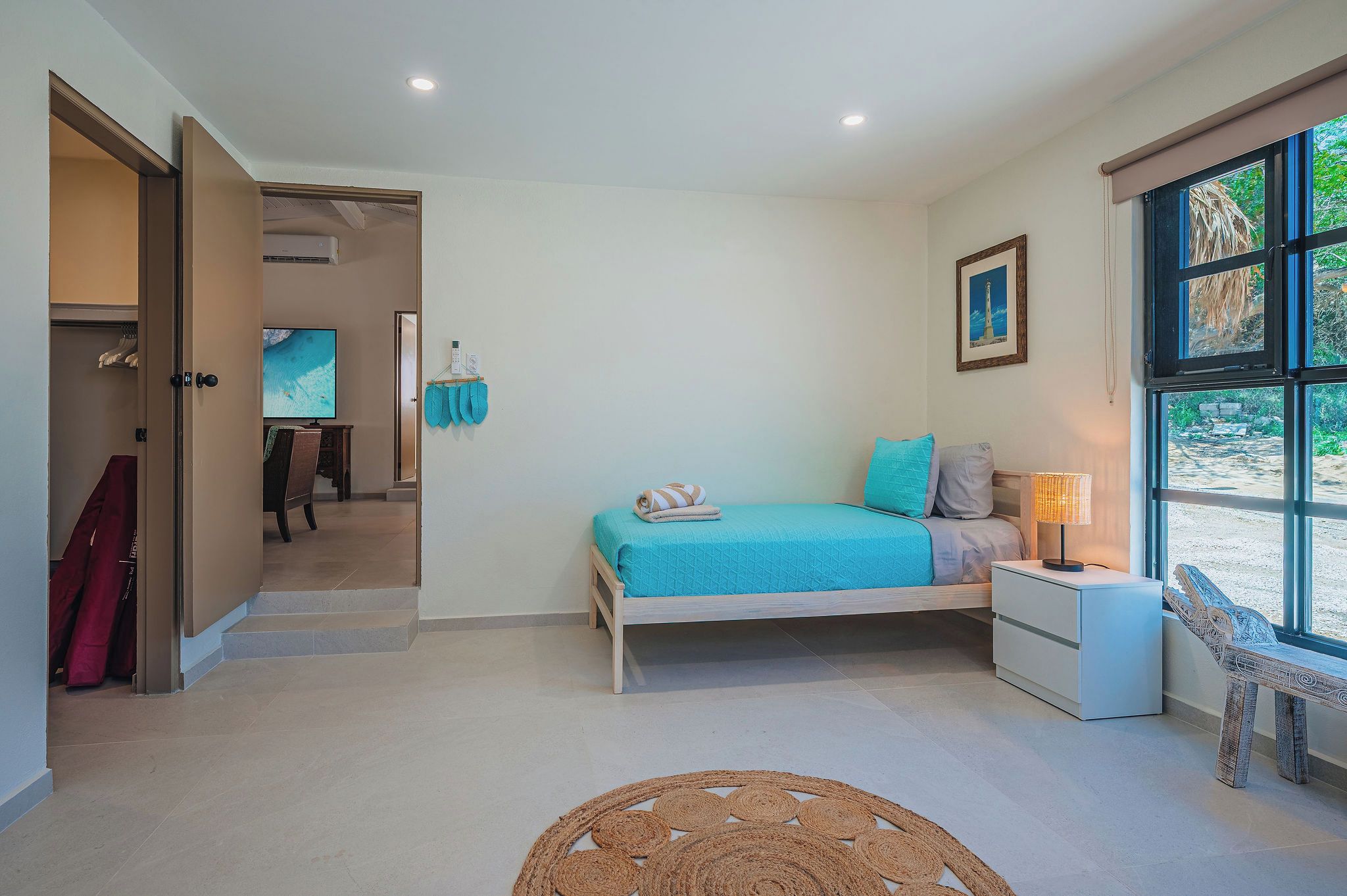 A bedroom with a bed, a nightstand, a window with a view, and a door leading to another room.