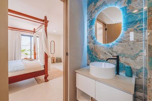 Ein Schlafzimmer mit einem Himmelbett, einem großen Spiegel und einem Badezimmer mit Marmorverkleidung und einem runden Waschbecken.