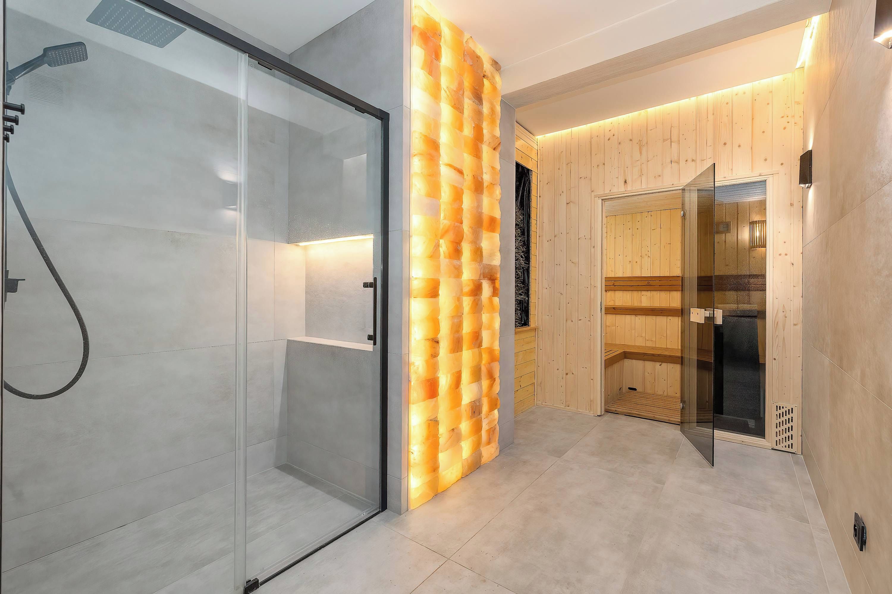 Een moderne badkamer met een glazen douchecabine, een sauna wand van hout en een sauna met houten banken.
