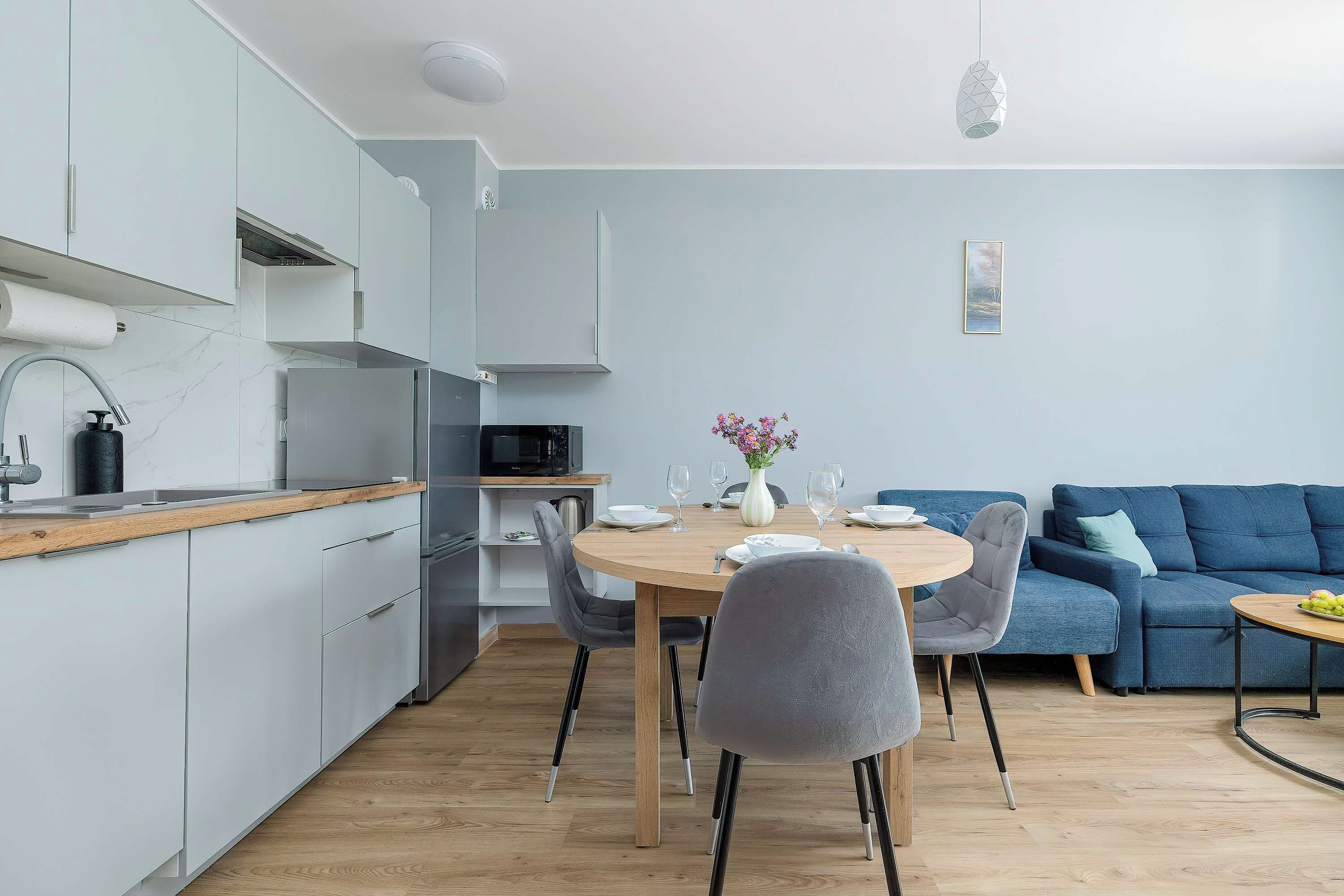 A modern kitchen with a dining area, a blue sofa, and a small table with a vase of flowers.