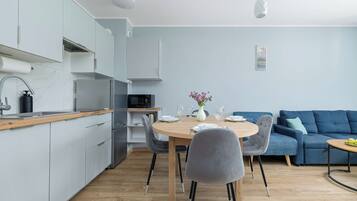 A modern kitchen with a dining area, a blue sofa, and a small table with a vase of flowers.