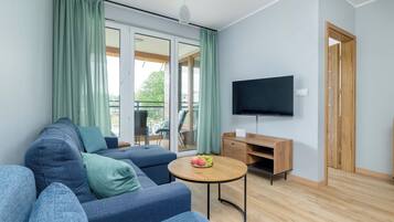 A modern living room with a sectional sofa, a coffee table with fruit, a flat-screen TV, and a sliding door leading to an outdoor area.