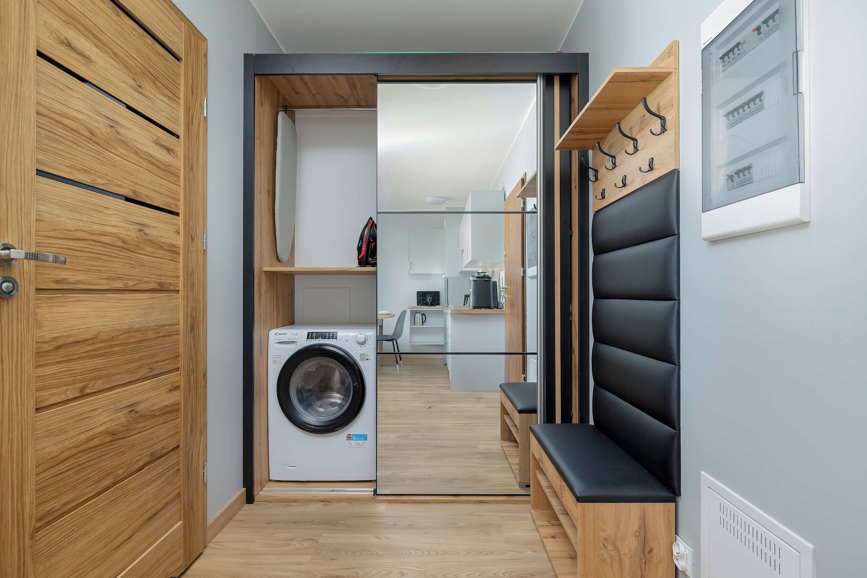 A modern laundry room with a washing machine, wooden cabinets, and a bench.
