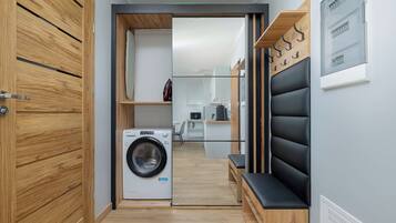 A modern laundry room with a washing machine, wooden cabinets, and a bench.