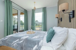 Une chambre à coucher comprenant un lit, une table de chevet, une lampe fixée au mur et une vue sur l’extérieur par une fenêtre.