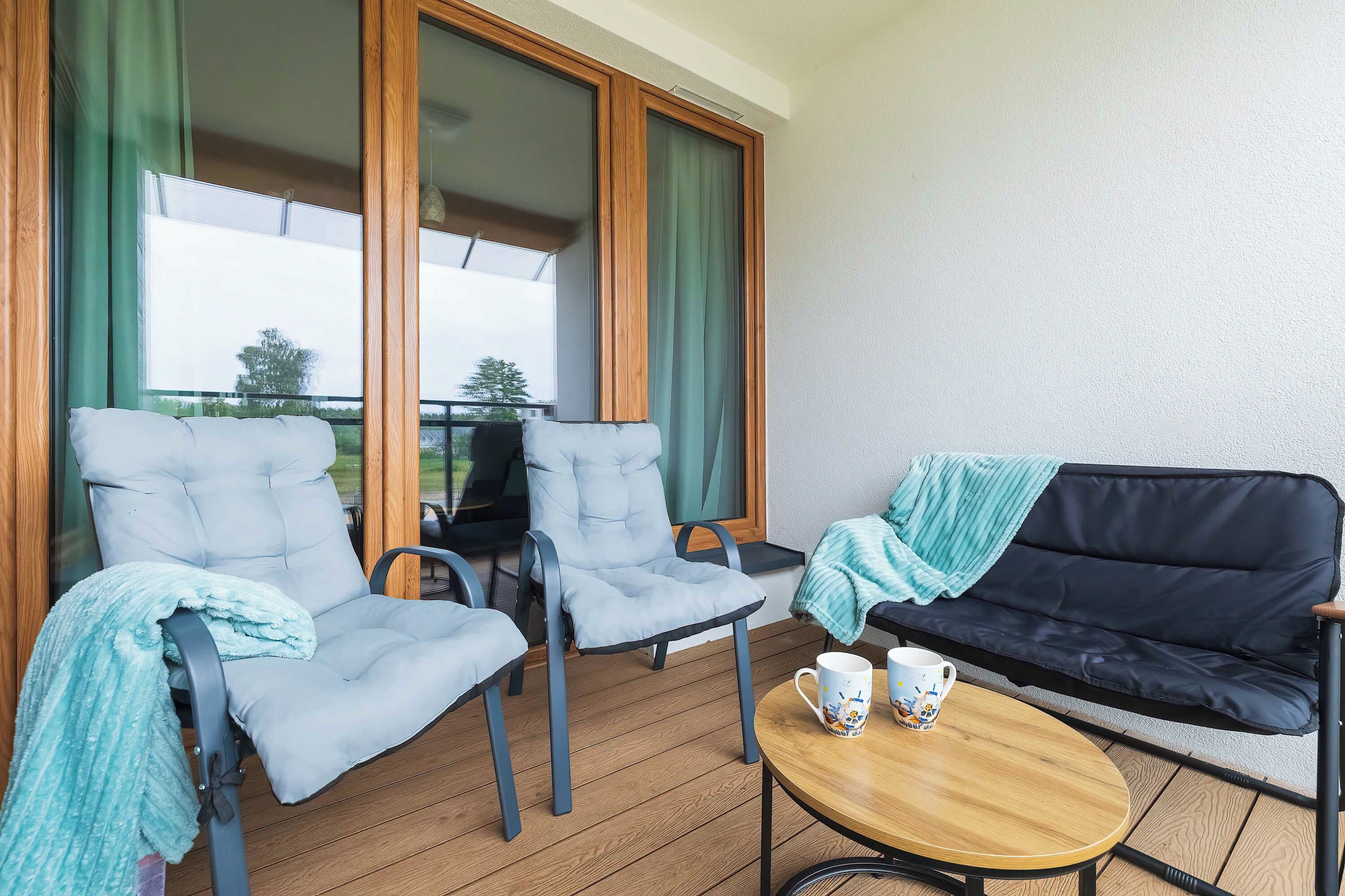 Een balkon met twee stoelen, een bank en een klein tafeltje met twee kopjes.