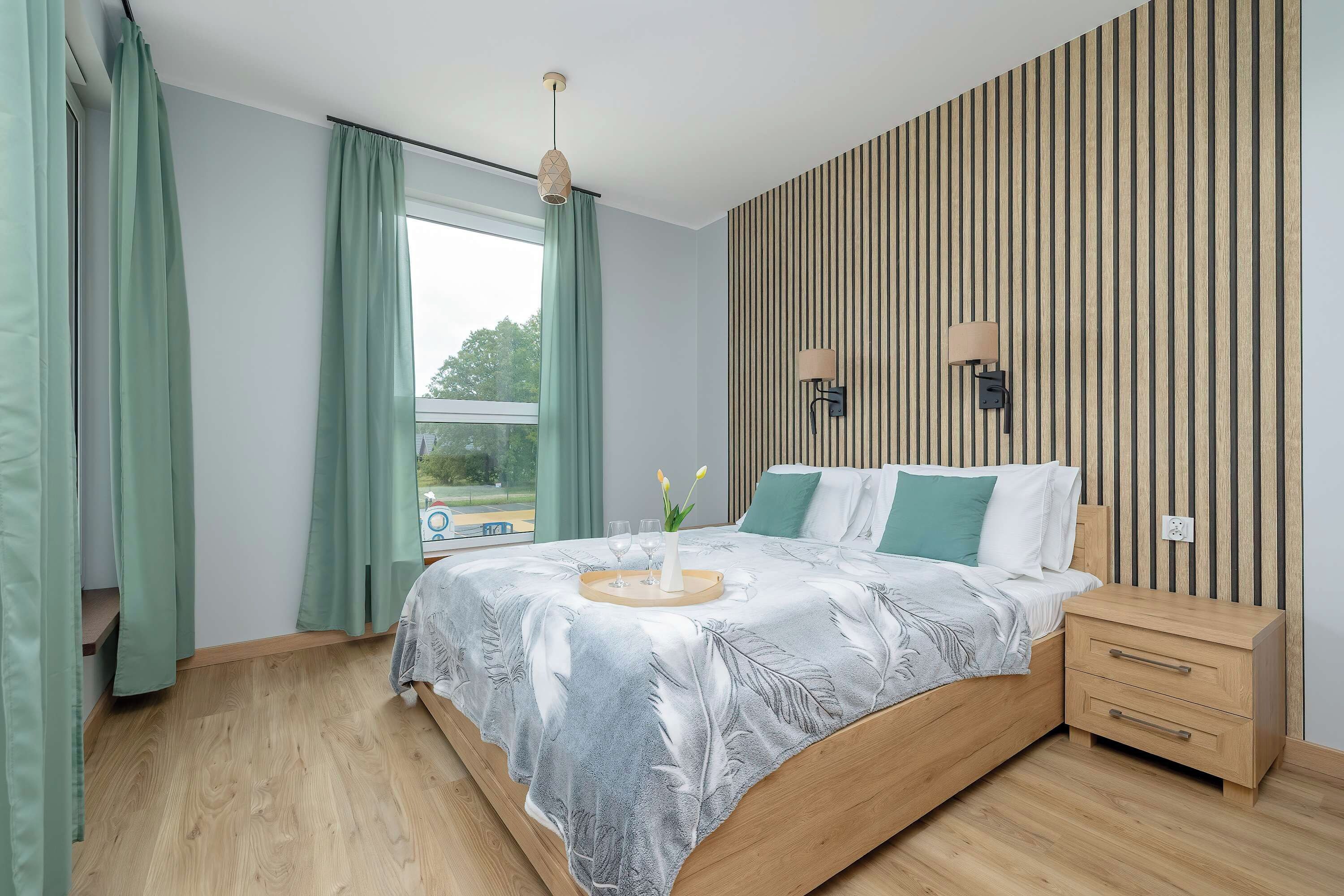 Ein modernes Schlafzimmer mit einem hölzernen Bett, einem Nachttisch, einem Fenster mit Vorhängen und einer Wandleuchte.