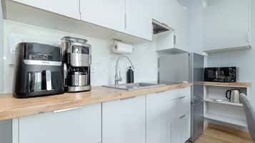 A modern kitchen with white cabinetry, a wooden countertop, a coffee maker, a kettle, and a microwave.
