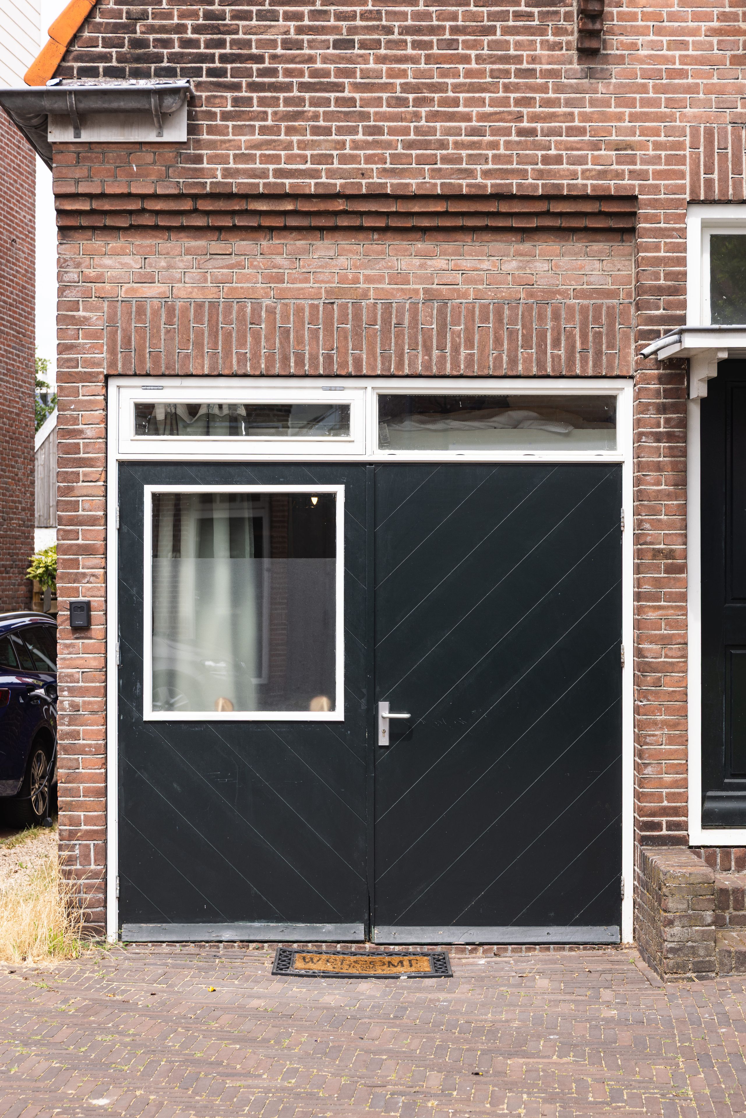 A black double door with a window, a mailbox, and a doormat with a nameplate.