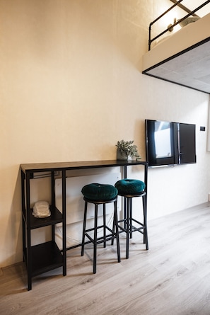 Eine moderne Küche mit einem schwarzen Metalltisch, zwei grünen gepolsterten Hocker, einer kleinen Topfpflanze und einem flachbildfernseher an der Wand.