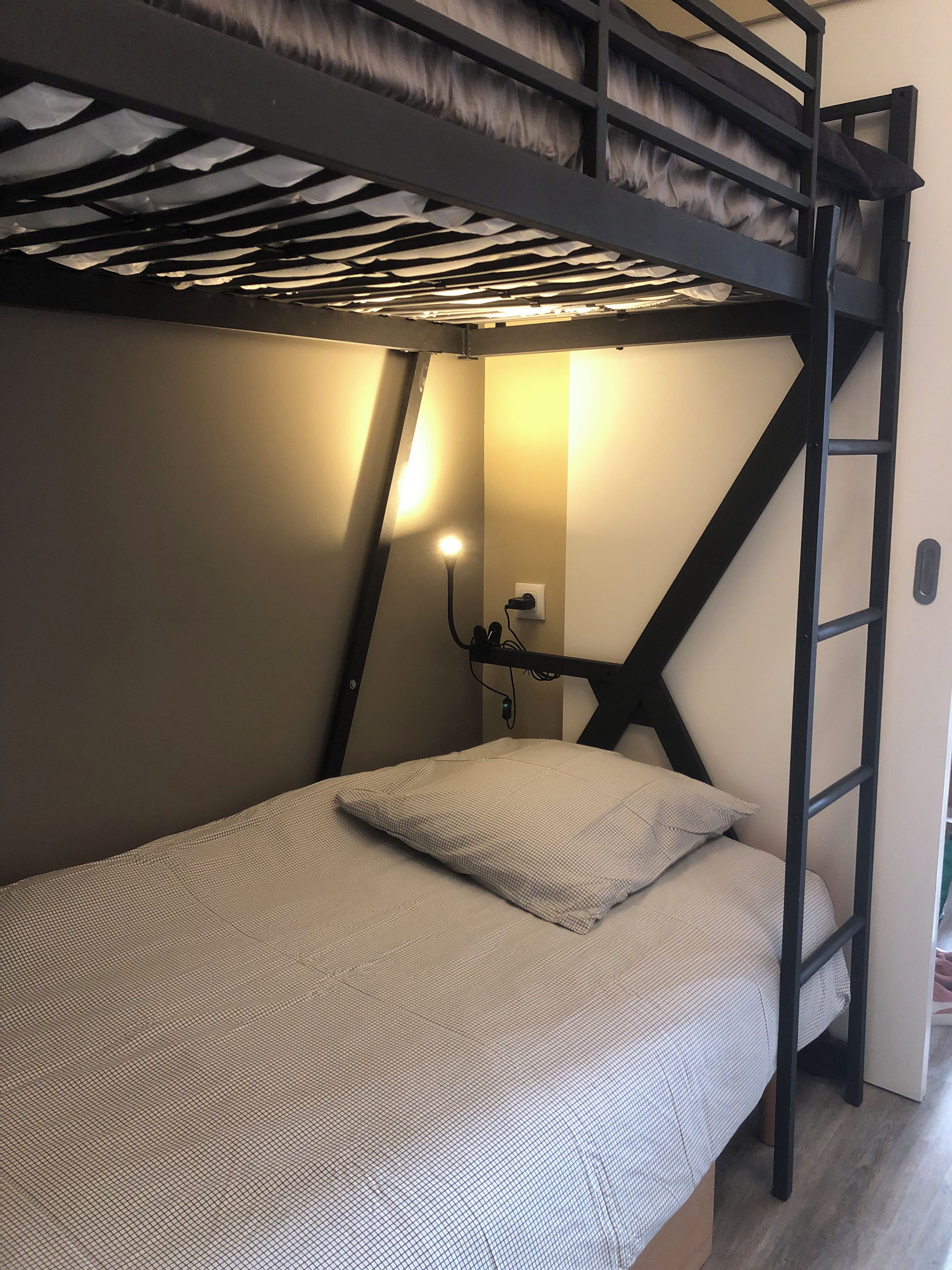 Una cama litera con escalera, una mesita de noche con lámpara y un enchufe de pared.