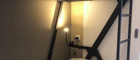 A bunk bed with a ladder, a bedside table with a lamp, and a wall socket.