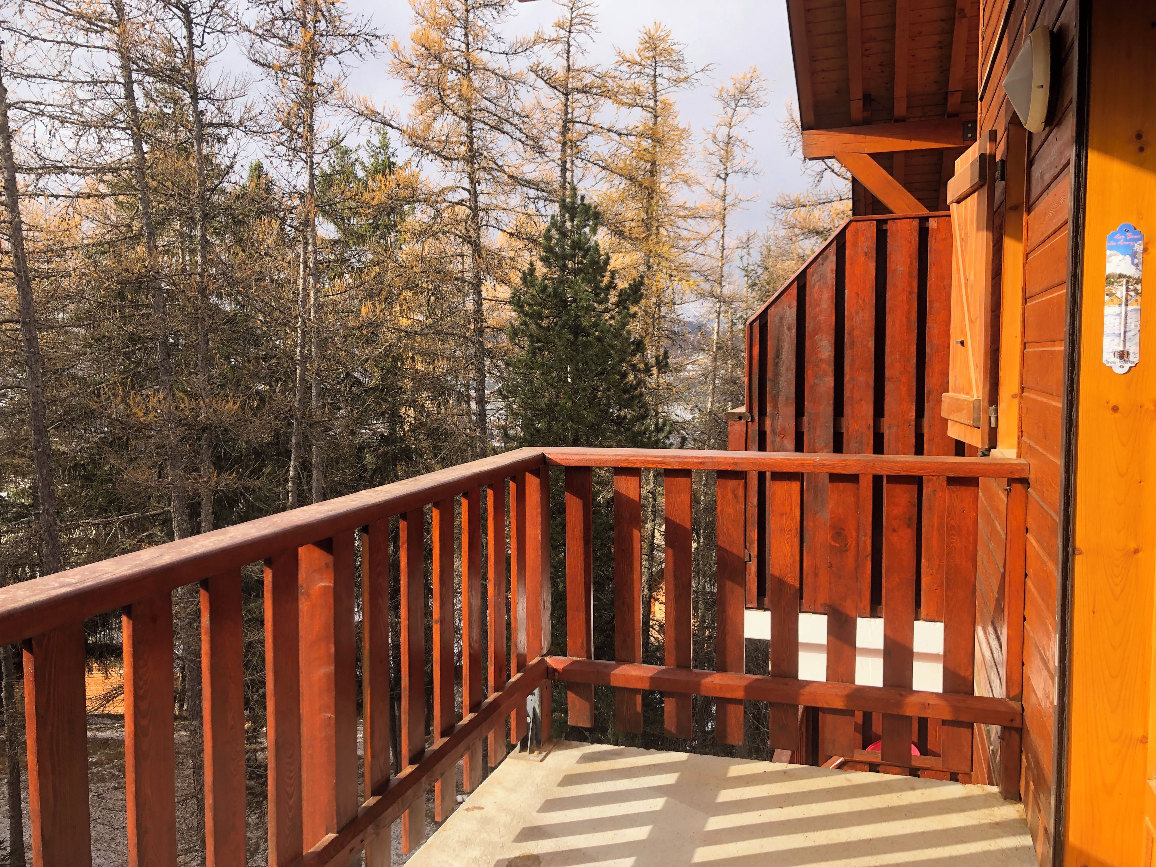 Un balcon en bois, doté d’une rambarde en métal, qui donne sur une zone boisée.