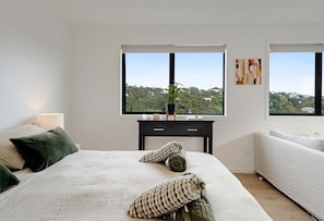 Une chambre à coucher avec un lit, une table de chevet, une fenêtre donnant sur une colline et un tableau accroché au mur.