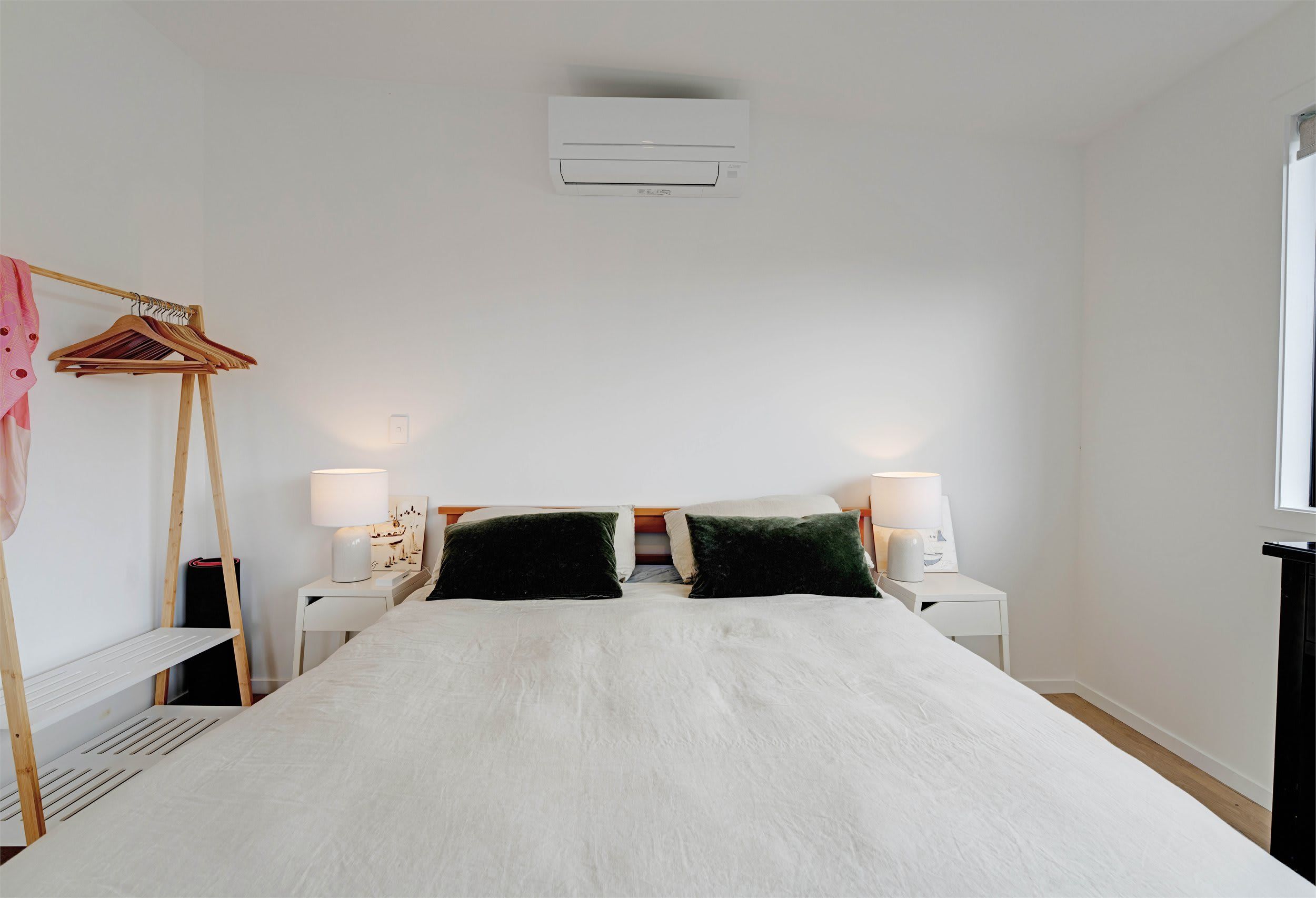 A bedroom with a bed, two bedside tables, a hanging light fixture, and a window.