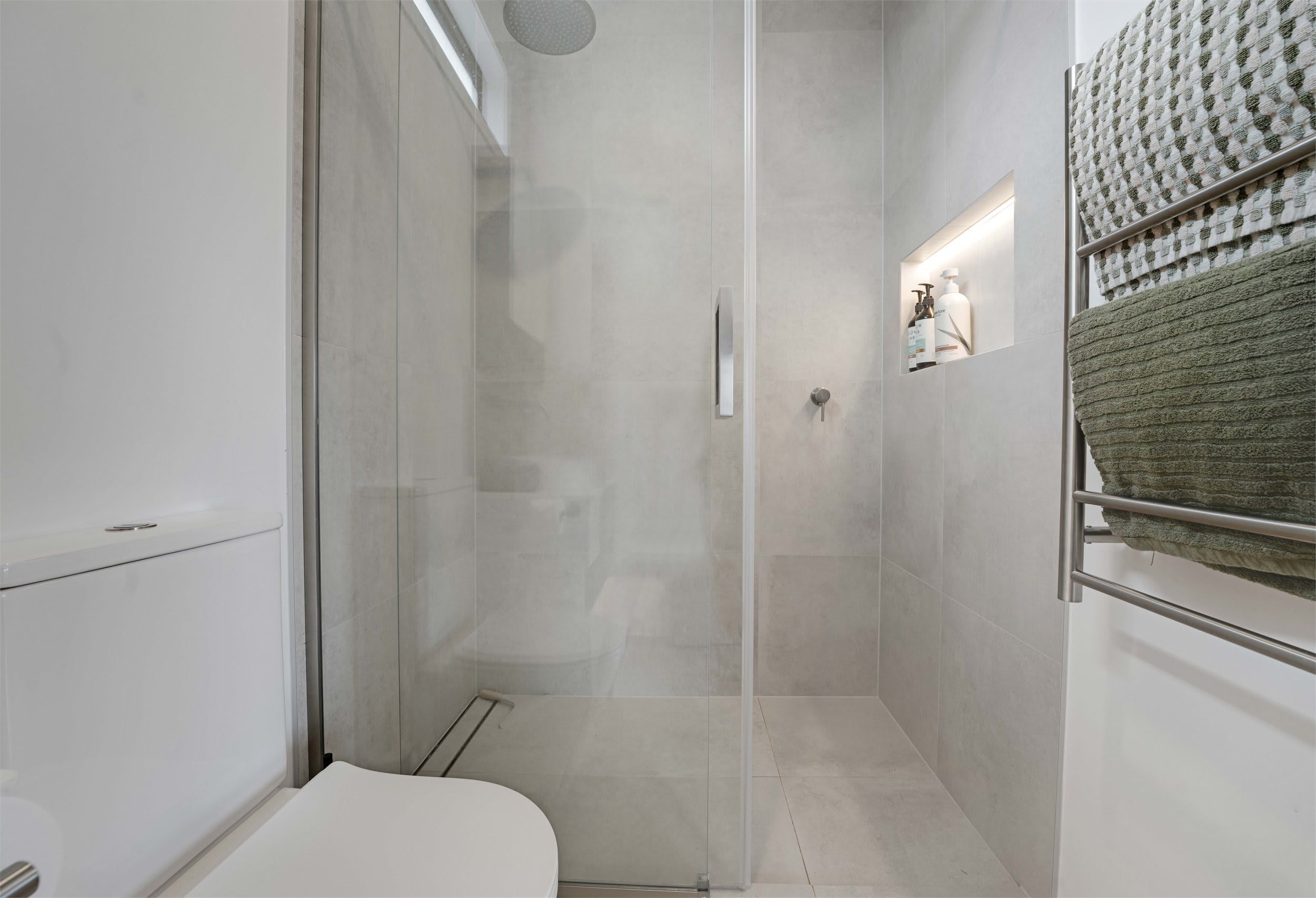 A modern bathroom with a glass shower enclosure, a toilet, and a towel rack with a folded towel.
