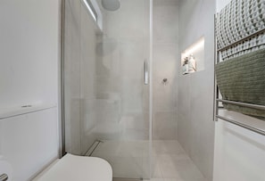 Une salle de bain moderne avec une douche à parois de verre, des toilettes et un porte-serviettes sur lequel est posée une serviette pliée.