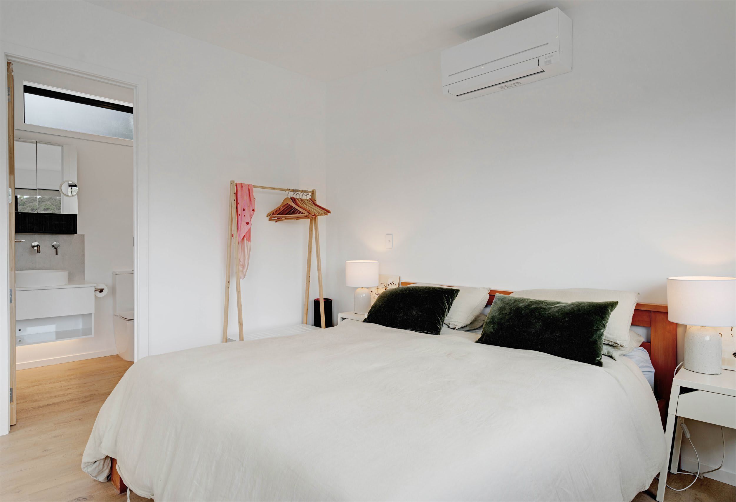 Ein Schlafzimmer mit einem Bett, Nachttischlampen, einem Kleiderständer und einer Wand-Klimaanlage.
