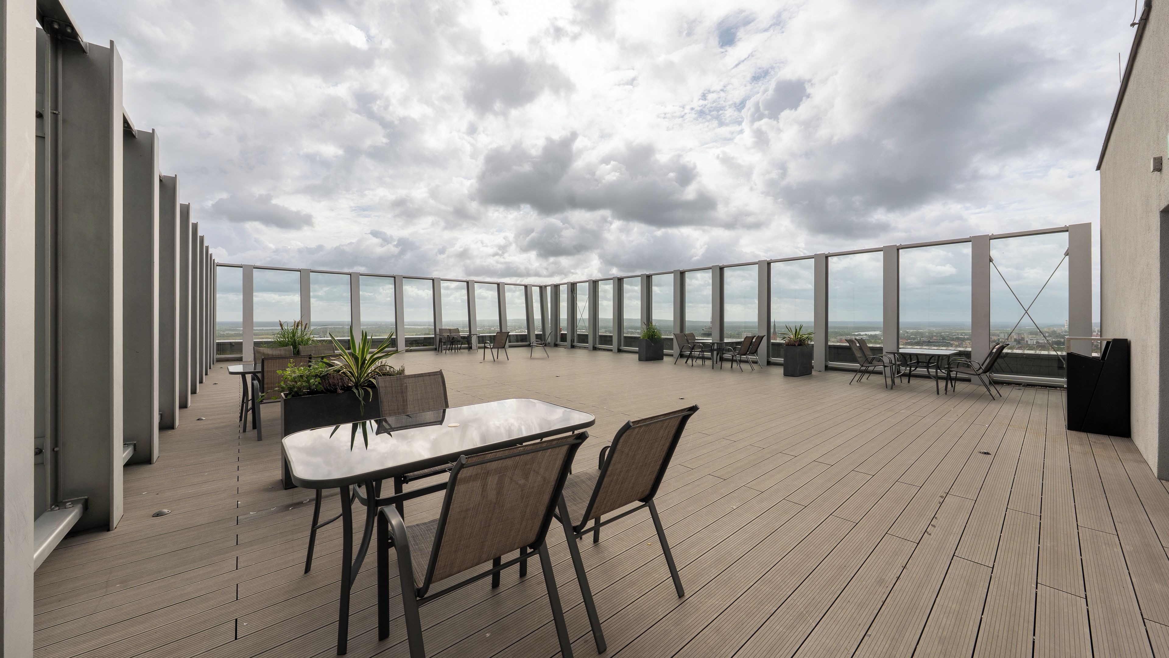 Une terrasse sur le toit avec une table et des chaises, de grandes fenêtres et des plantes en pot.
