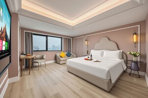 A modern hotel room with a large bed, a desk, and a television displaying a cityscape.