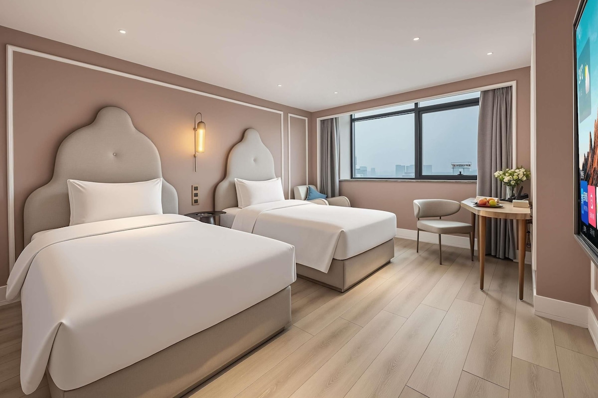 Habitación de hotel con dos camas, un escritorio, una silla y un ventanal grande.