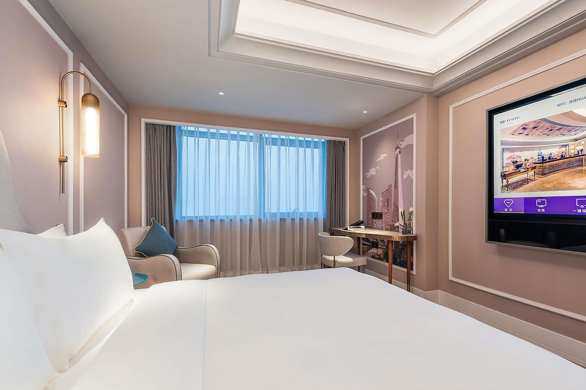 Habitación de hotel con una cama grande, un escritorio, una silla y un televisor en la pared.