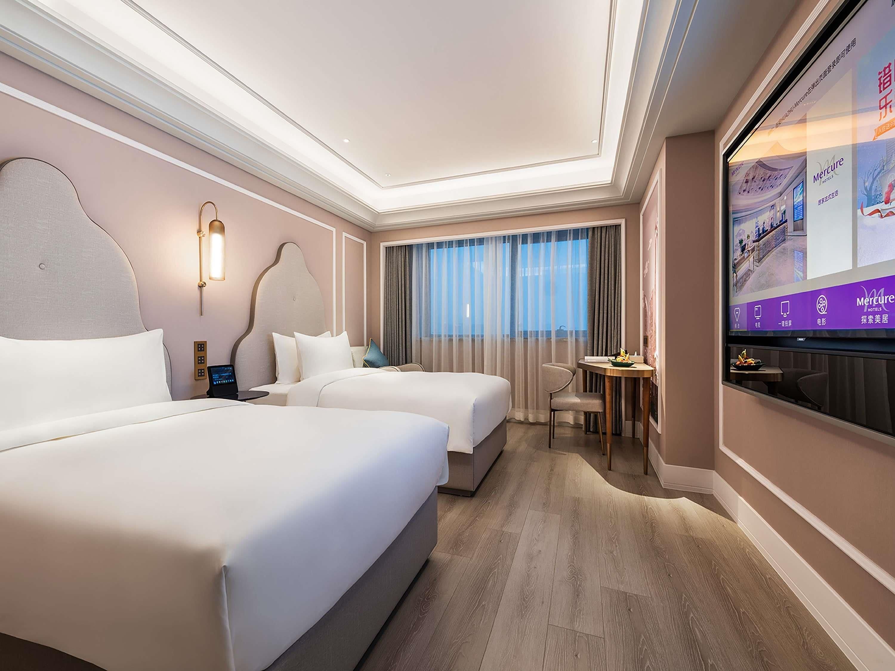Une chambre d’hôtel équipée de deux lits, d’un bureau, d’une chaise et d’un écran de télévision affichant des informations sur l’hôtel.
