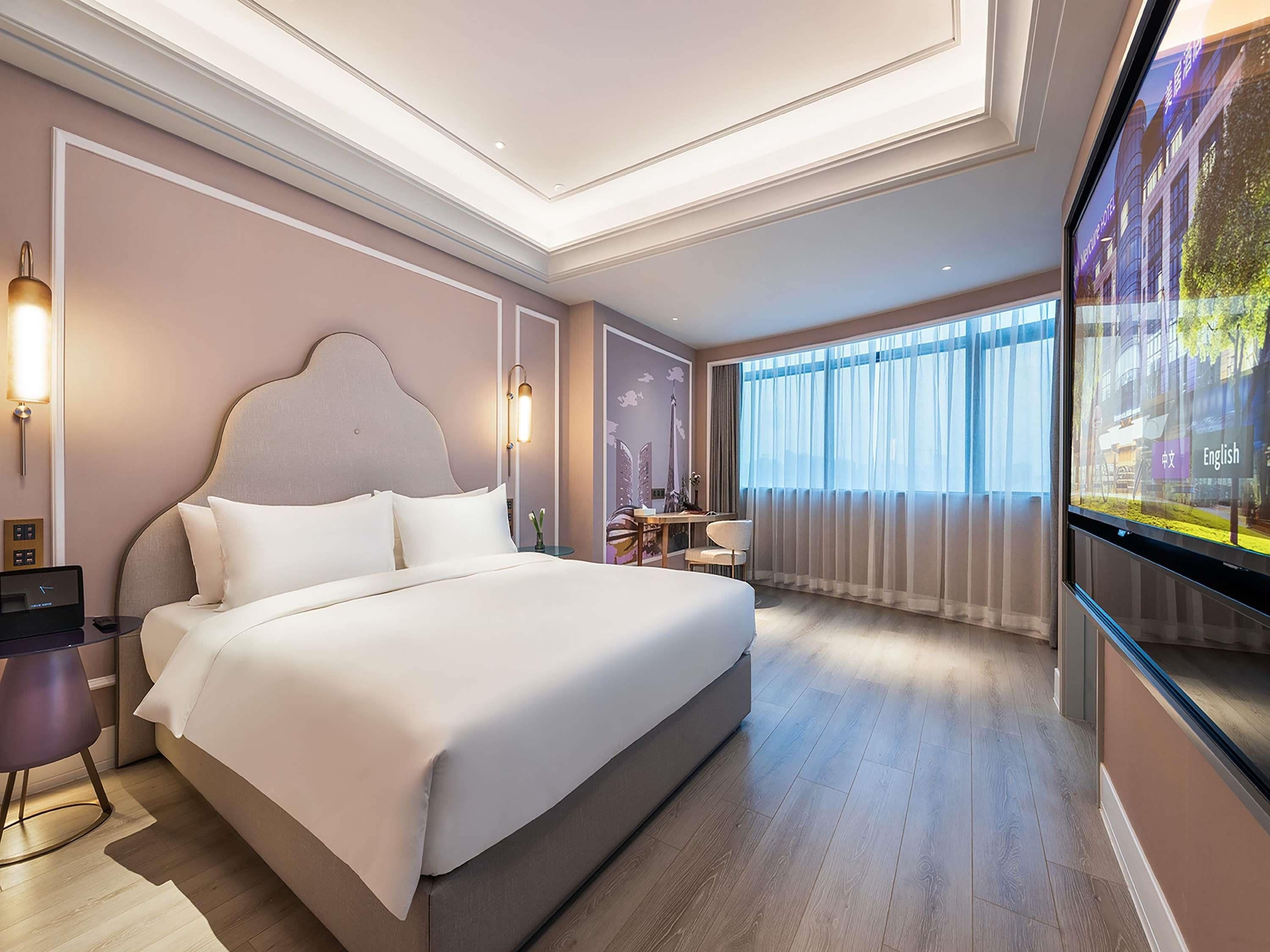 Une chambre d’hôtel moderne avec un grand lit, des tables de chevet, un bureau et une grande fenêtre avec des rideaux.