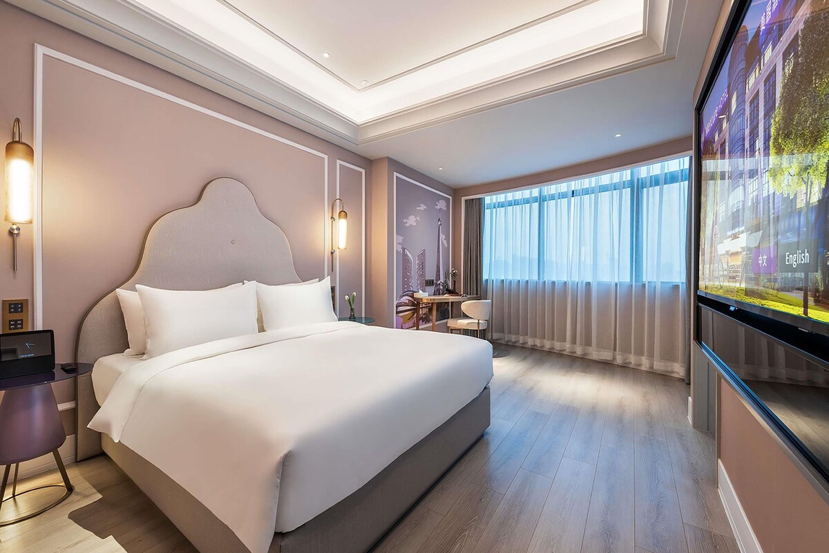 Habitación de hotel moderna con una cama grande, mesitas de noche, un escritorio y un ventanal con cortinas.