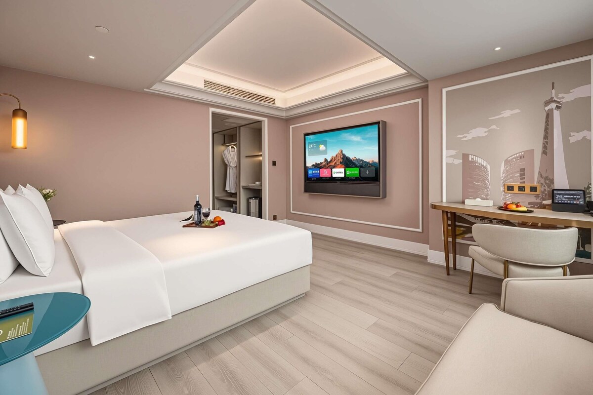 Una habitación de hotel moderna con una cama, un escritorio con computadora, un televisor y un armario.